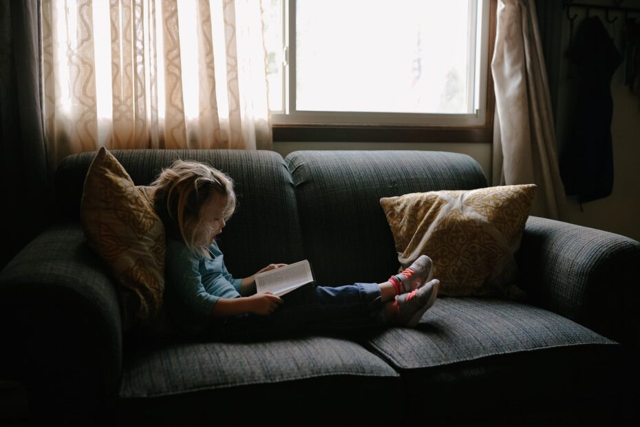 Une petite fille assise sur un canapé fuit le dérangement intérieur en lisant un livre.