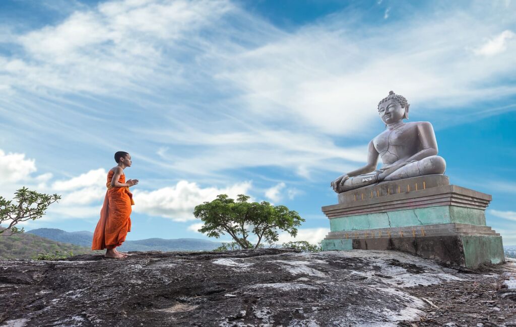 un moine dans la joie d'être soi priant le renouveau devant une statue de bouddha