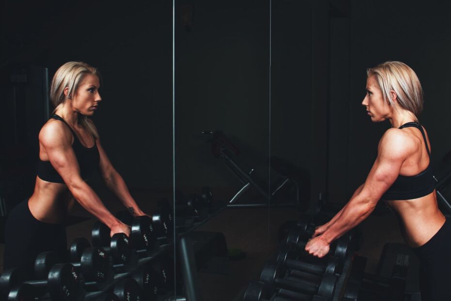 Une femme blonde utilise la technique de défocalisation mentale devant le miroir d'une salle de sport.