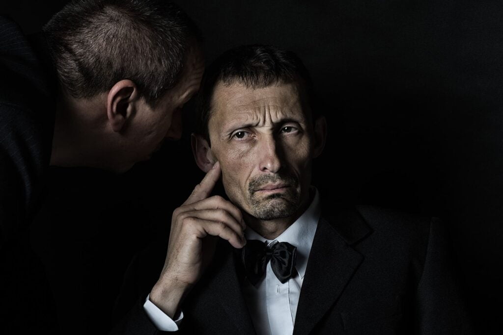Un homme tend l'oreille pour écouter un autre homme lui parler. L'écoute est une base primordiale de la communication et fait partie des 9 règles d'or !